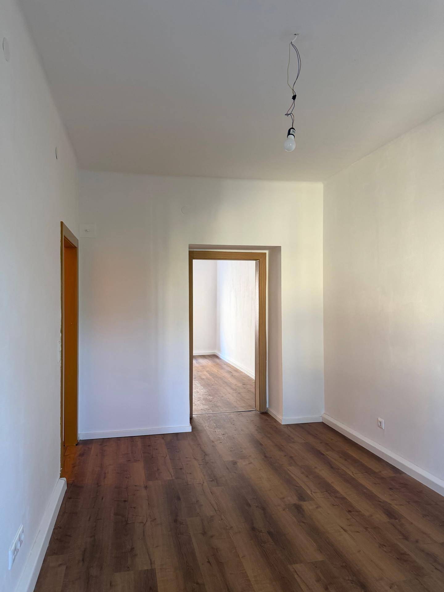 Leeres Zimmer mit Laminatboden und einer breiten Türöffnung, die zu einem weiteren Raum führt.