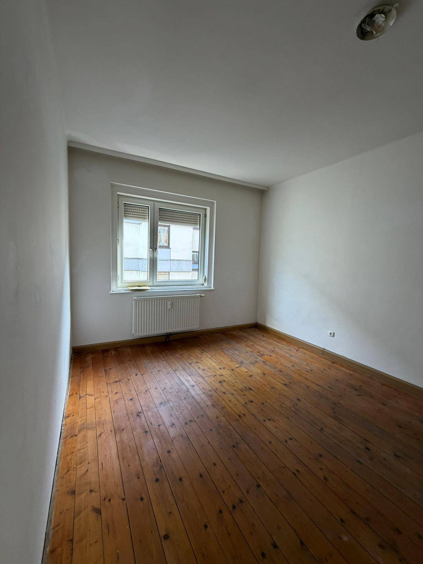 Helles Zimmer mit Dielenboden und Fenster mit Jalousien, ideal als Schlaf- oder Kinderzimmer.