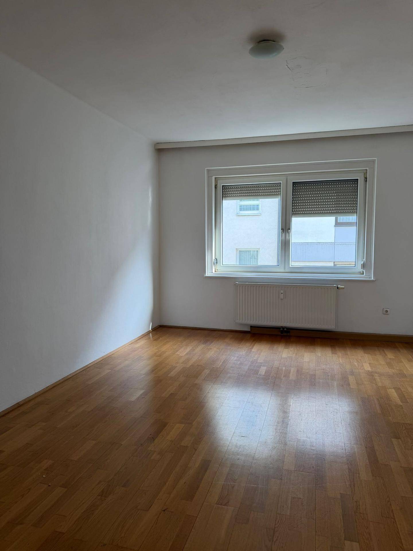 Geräumiges Zimmer mit Parkettboden und Fenster mit Jalousien, bietet viel Tageslicht.