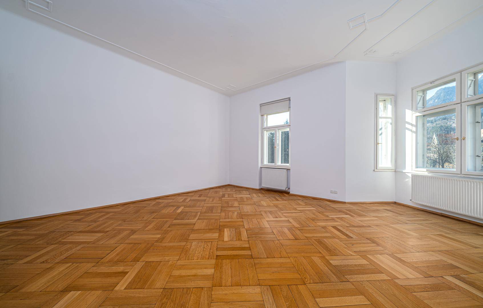 Heller Raum mit Parkettboden, hohen Decken und Fenstern mit Bergblick.