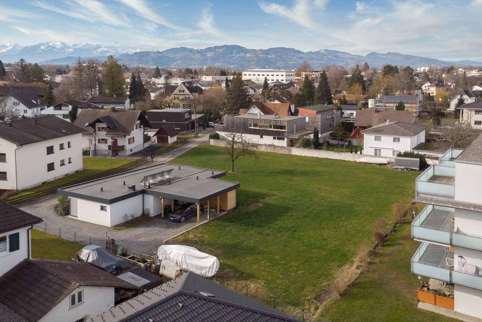 Panoramablick aus der Vogelperspektive auf das Grundstück mit umliegenden Häusern und Bergkette.