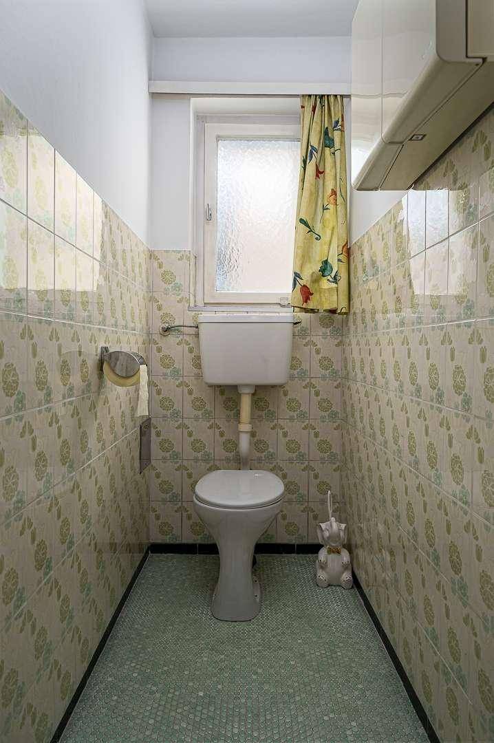 Separate Toilette mit gemusterten Fliesen, Fenster und traditioneller Einrichtung.