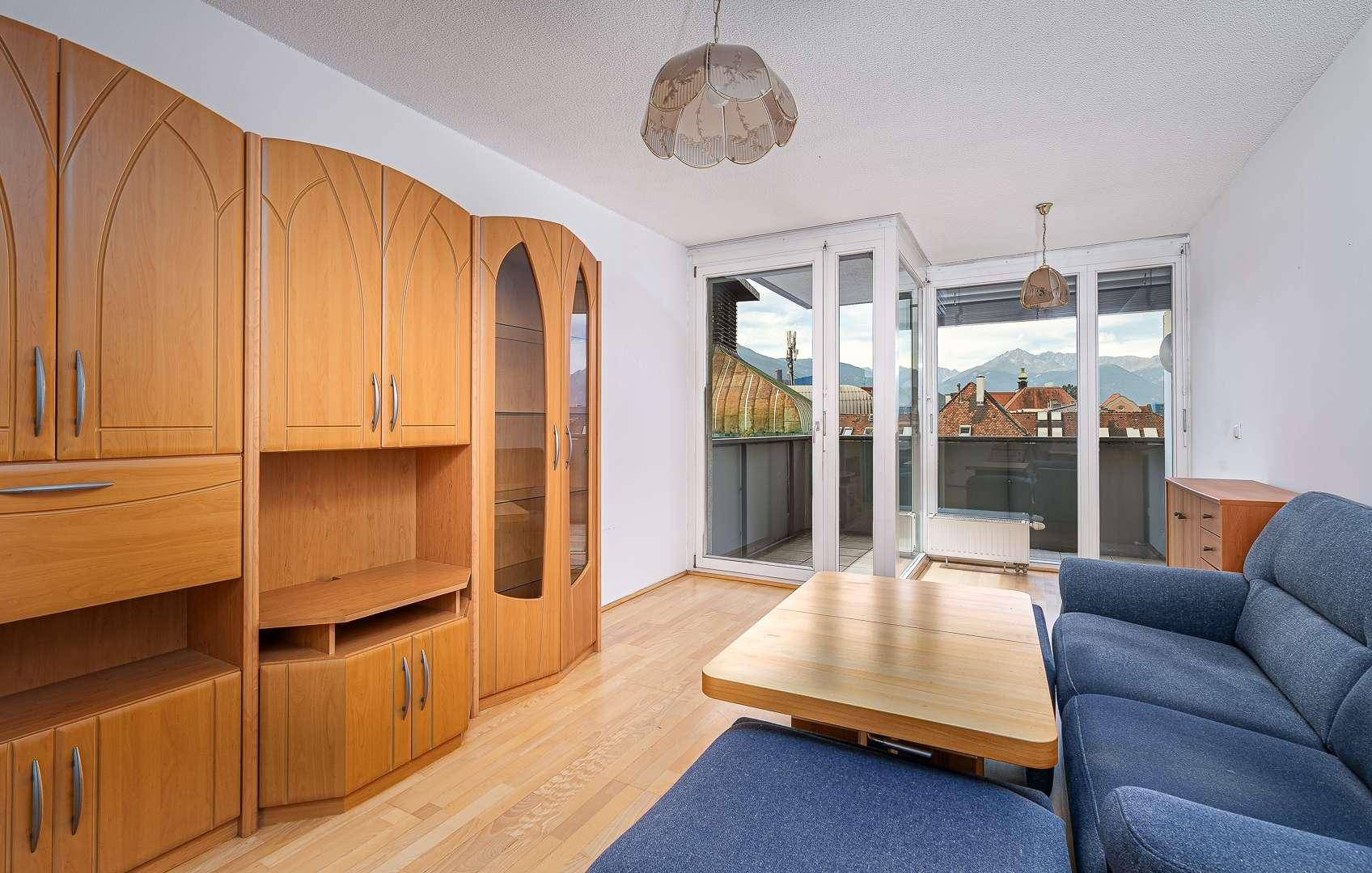 Gemütliches Wohnzimmer mit Holzmöbeln, Parkettboden und Zugang zum Balkon mit Bergblick.