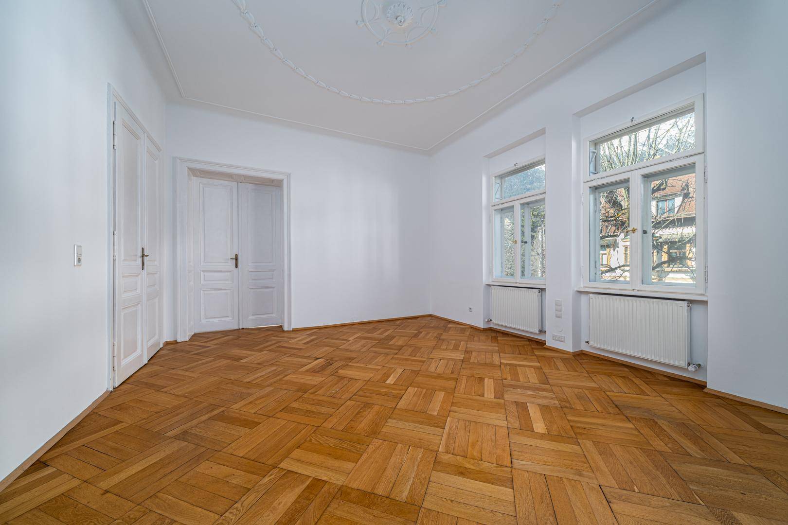 Geräumiges Schlafzimmer mit Parkettboden, Stuckdecke und großen Fenstern.