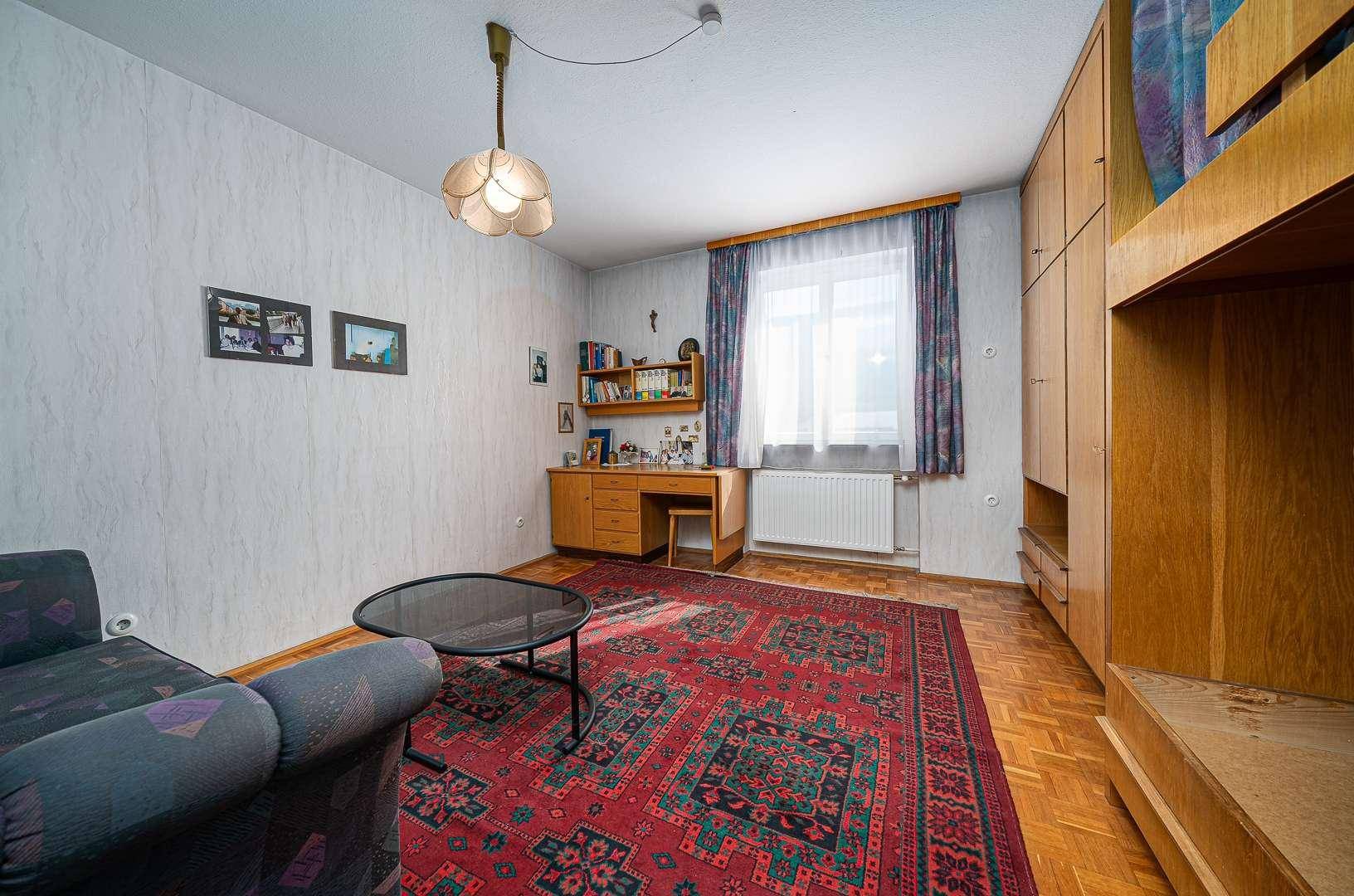 Schlafzimmer mit Holzmöbeln, Teppich und einem Schreibtisch am Fenster.