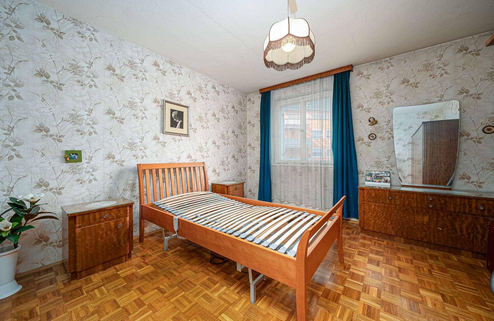 Schlafzimmer mit Einzelbett, Holzmöbeln und gemusterter Tapete.