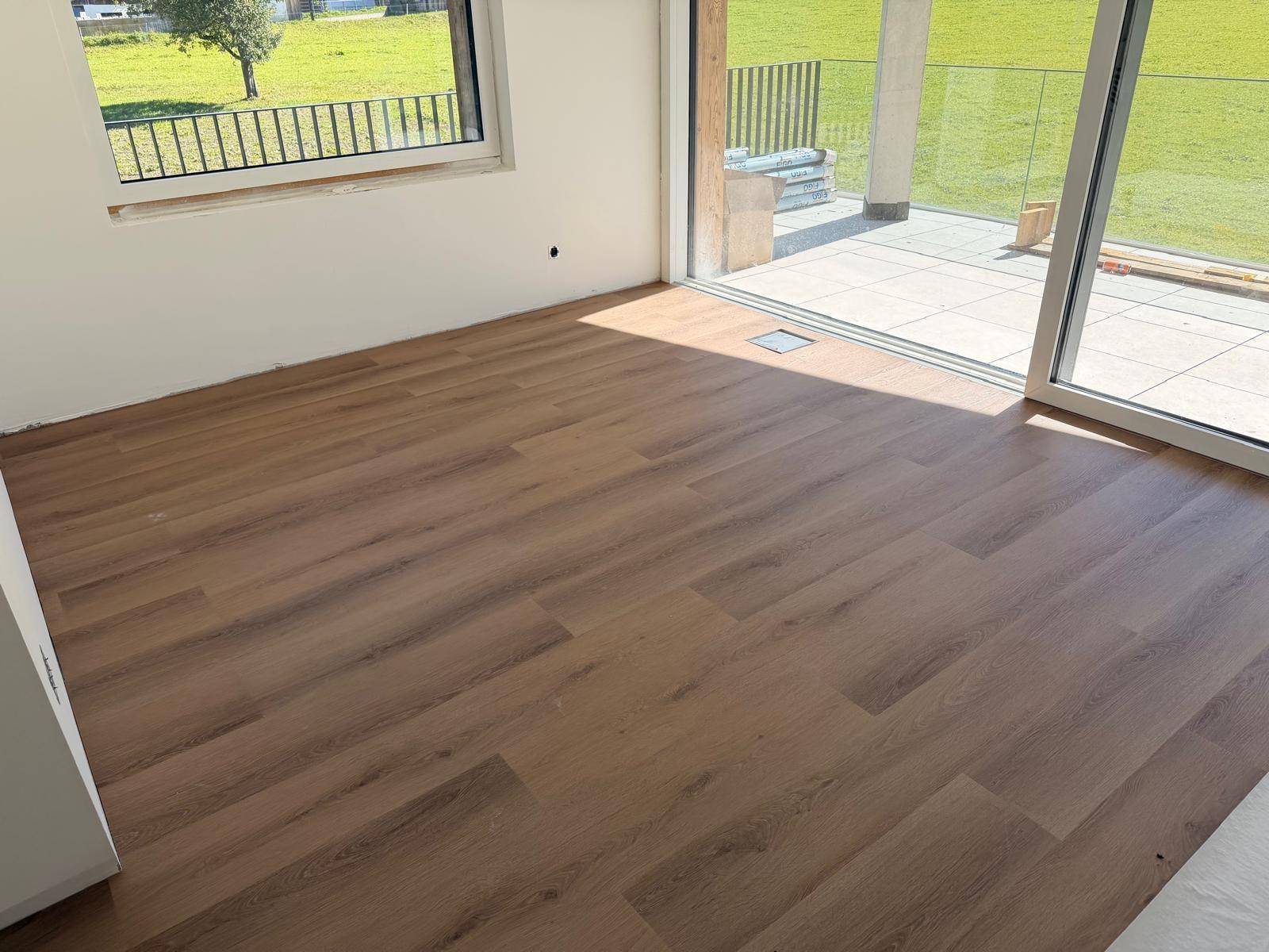Heller Raum mit neuem Laminatboden, großen Fenstern und Zugang zur Terrasse mit Grünblick.