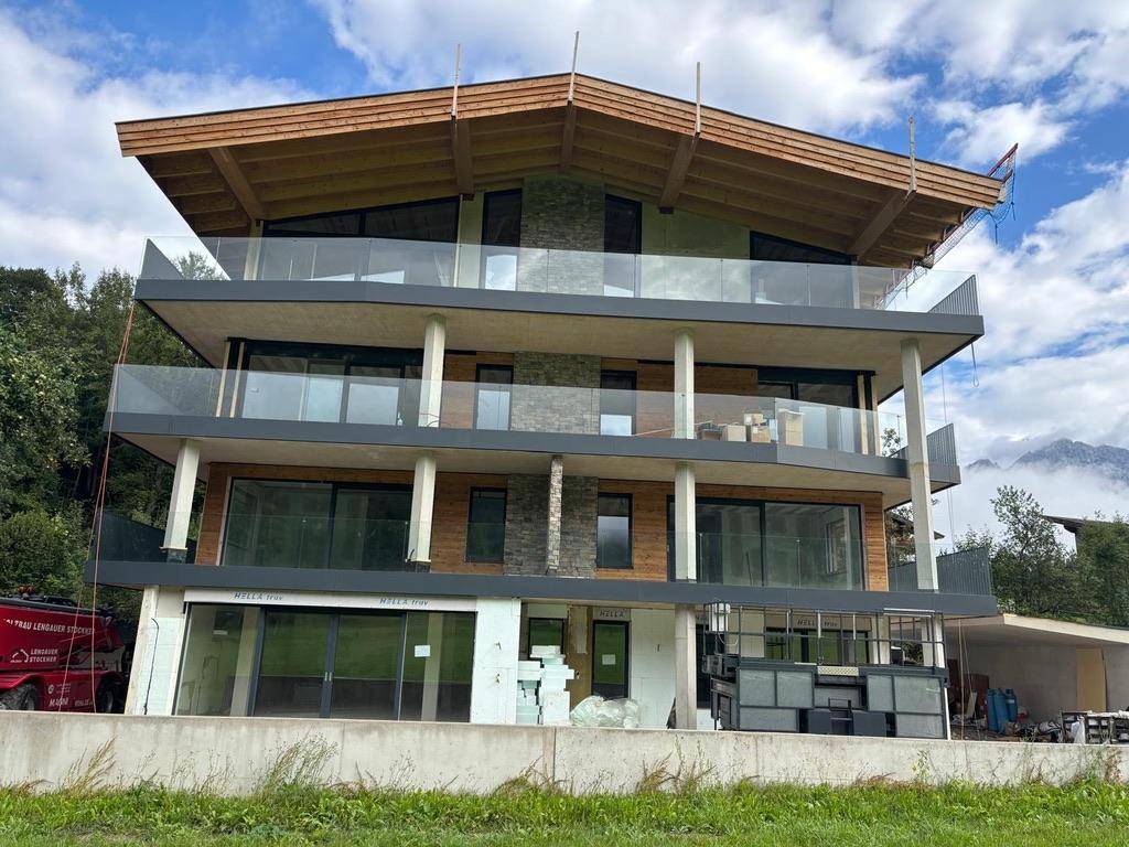 Modernes Mehrfamilienhaus im Bau mit großen Glasfronten, Holzfassade und Bergblick.
