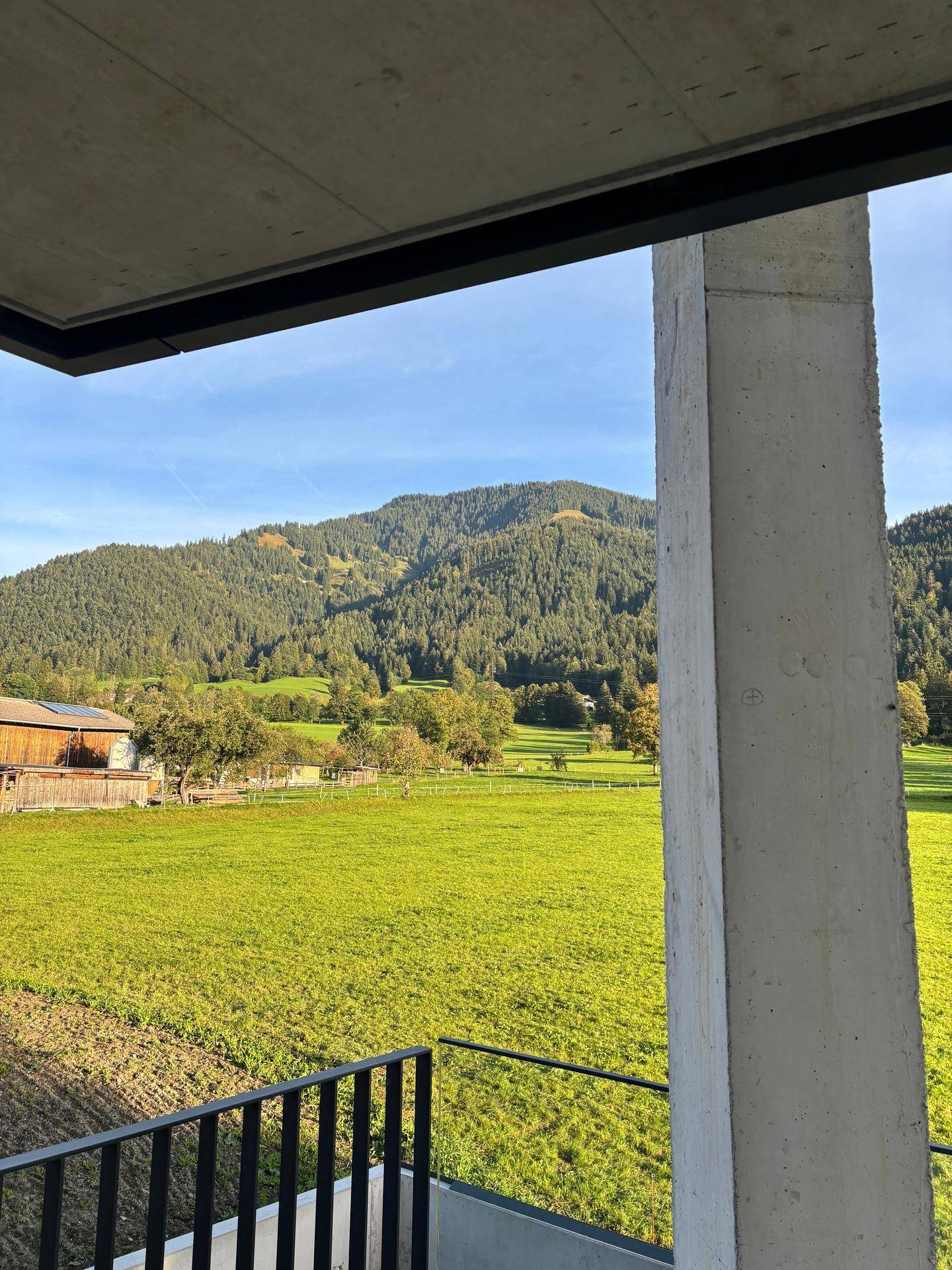 Weitläufiger Blick von einem Balkon über grüne Felder zu den bewaldeten Berghängen.