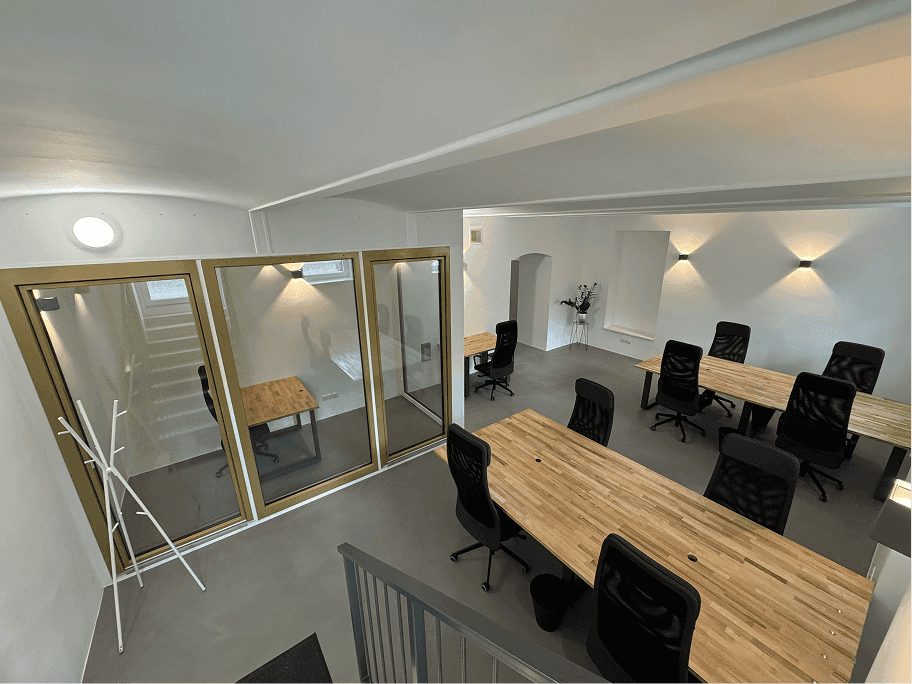 Weitläufiger Bürobereich mit mehreren Arbeitsplätzen, Glasabtrennungen und einer Treppe im Hintergrund.