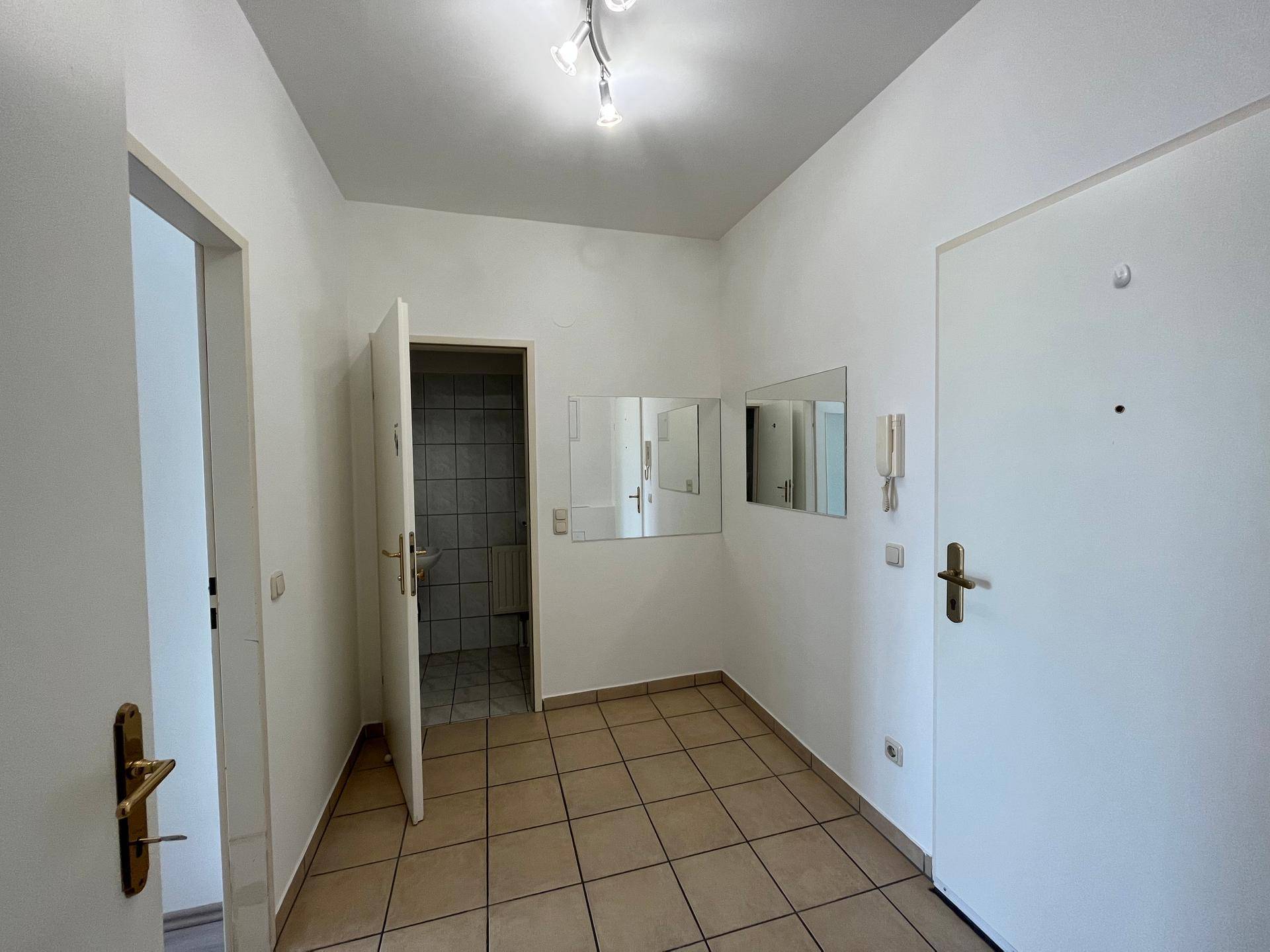 Heller Eingangsbereich mit Fliesenboden und Zugang zu weiteren Räumen, inklusive Badezimmer.