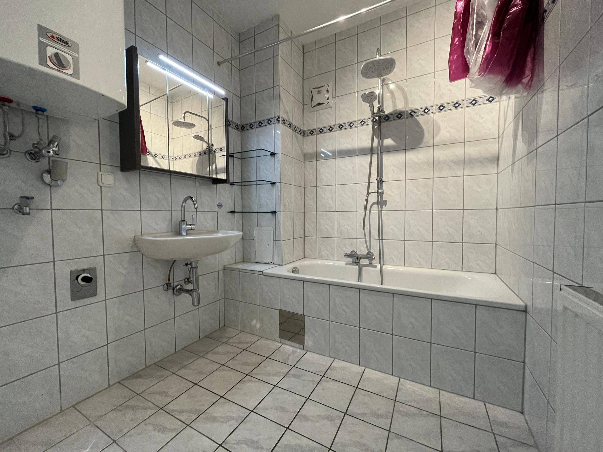 Gefliestes Badezimmer mit Badewanne, Dusche und Waschbecken, ausgestattet mit einem Spiegelschrank.