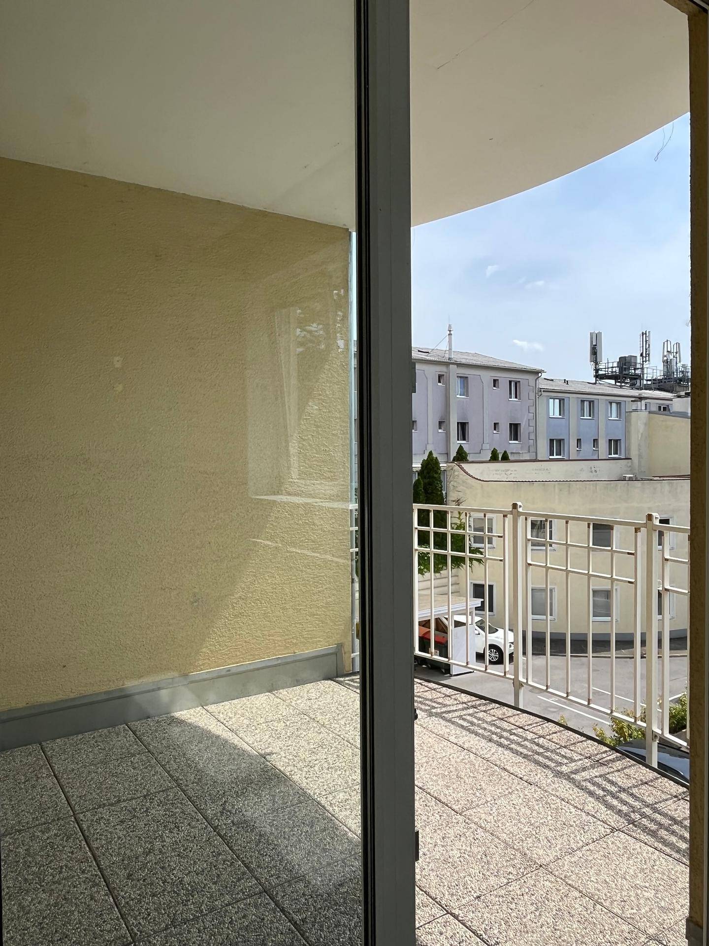 Balkon mit Fliesenboden und Blick auf die umliegende Bebauung und den Himmel.