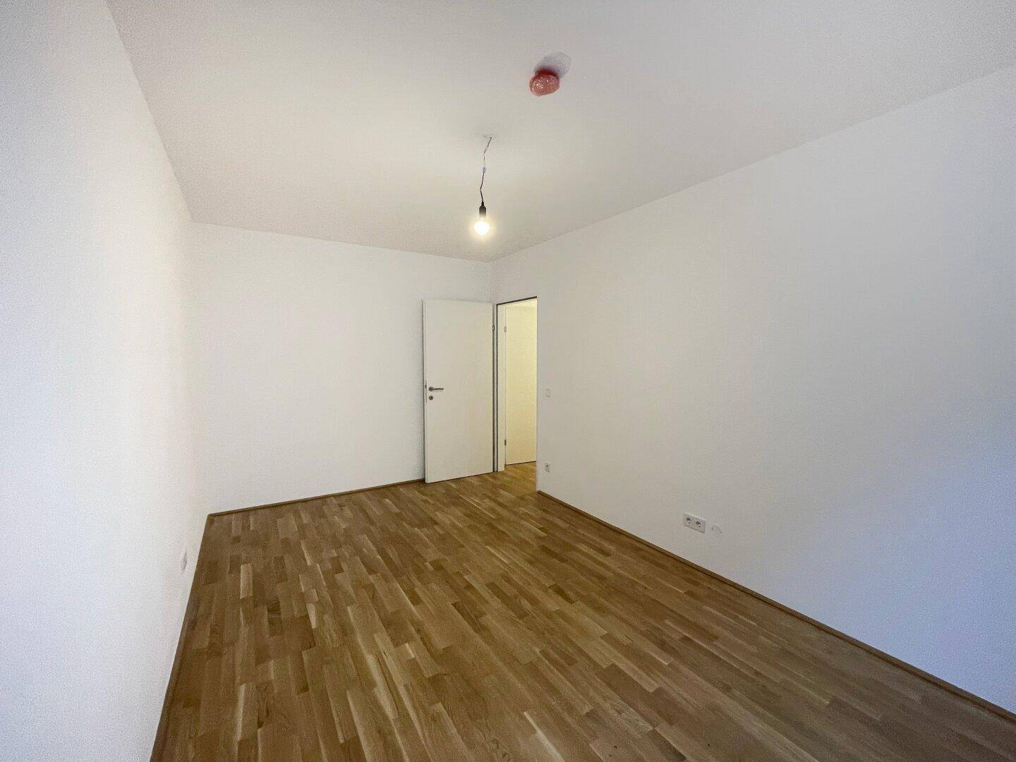 Leeres Schlafzimmer mit hellem Parkettboden und weiß gestrichenen Wänden, ideal für individuelle Einrichtung.