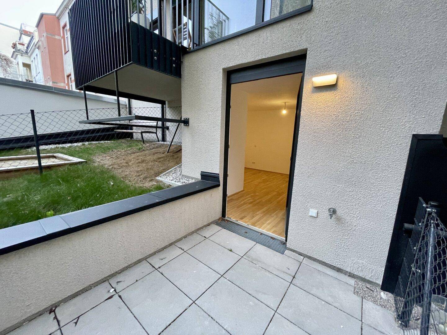 Unmöblierte Terrasse mit hellem Fliesenboden und Zugang zu einem leeren Innenraum mit Parkett.