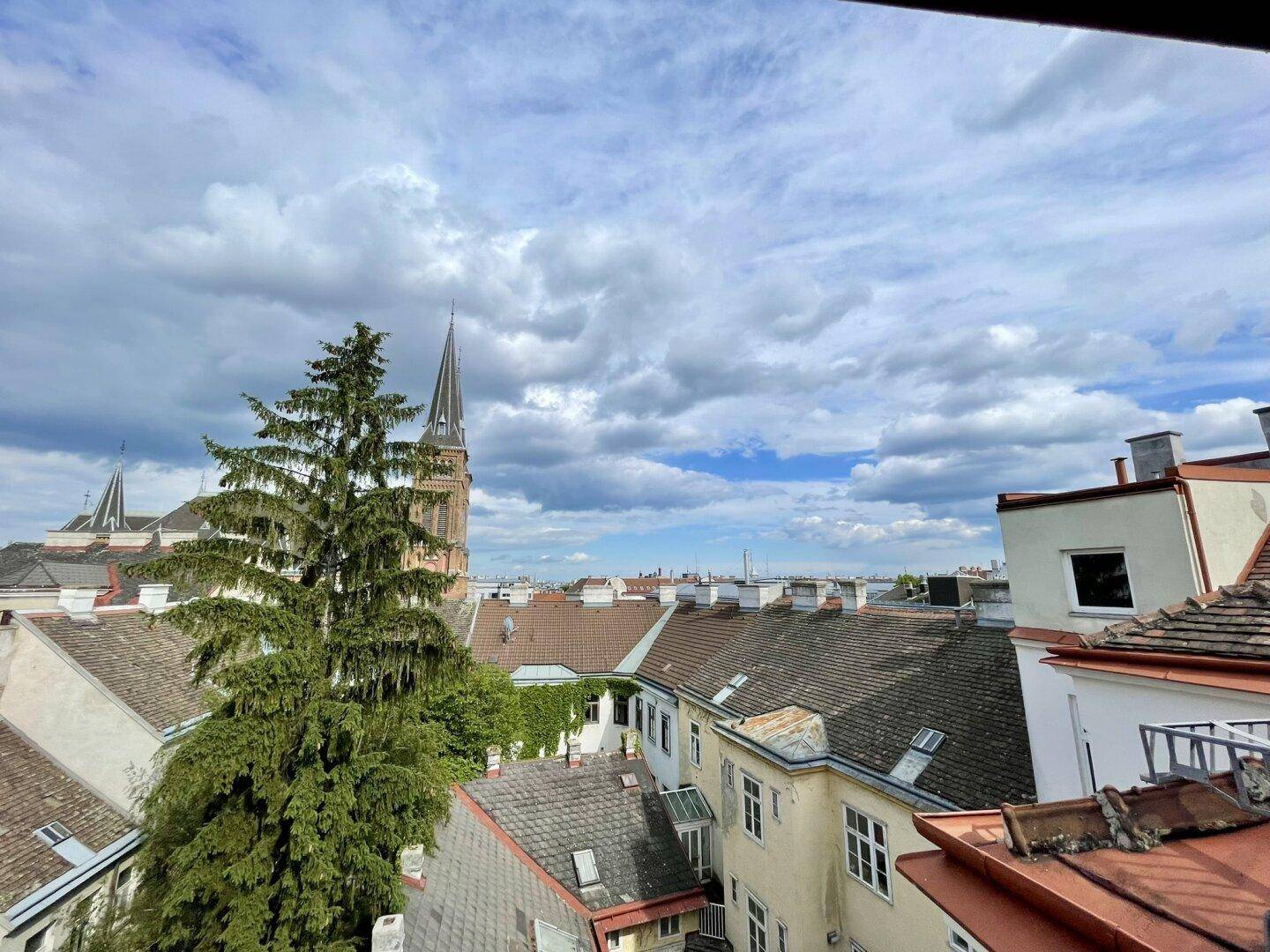 Weitläufiger Ausblick auf die städtische Dachlandschaft mit einem markanten Kirchturm und Wolken.