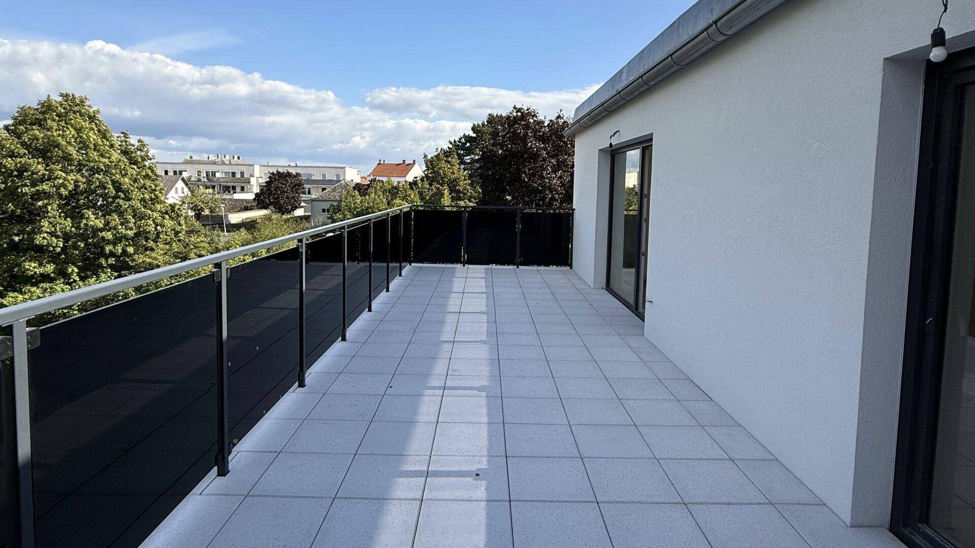 Weitläufige Dachterrasse mit Fliesenboden und moderner Brüstung, bietet viel Platz im Freien.