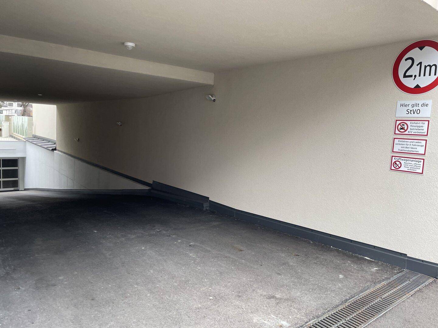 Einfahrt zur Tiefgarage mit Rampe, Höhenbegrenzung von 2,1 Metern und Überwachungskamera.