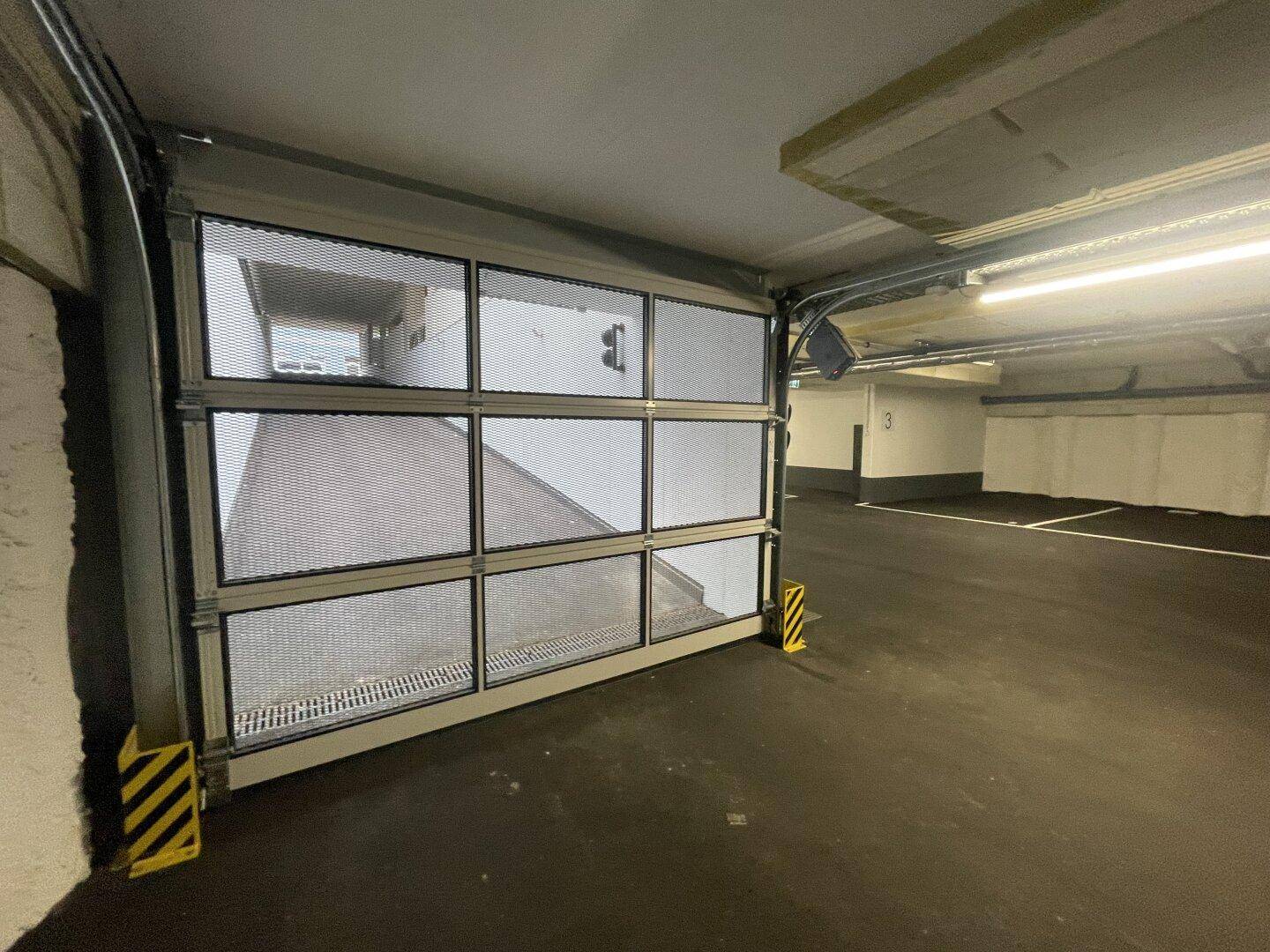 Blick in die Tiefgarage mit teilweise geöffnetem, modernem Garagentor und sauberem Betonboden.