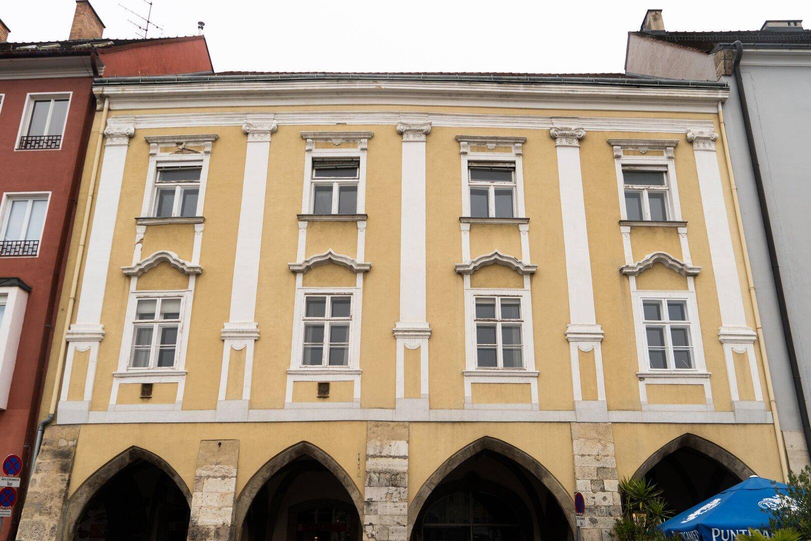 Historisches Gebäude mit gelber Fassade, weißen Säulen und Bögen im Erdgeschoss, das eine traditionelle Architektur aufweist.