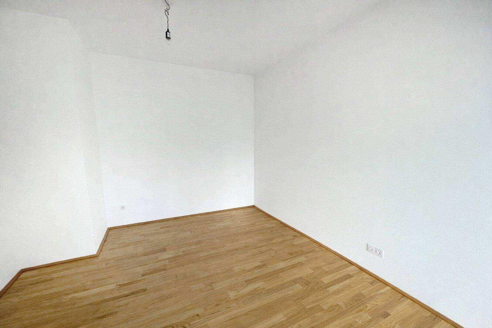 Heller, leerer Raum mit Holzboden und weißen Wänden, ideal für ein Kinderzimmer oder Büro.