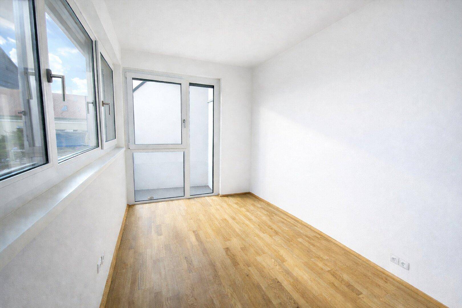 Heller Raum mit Holzboden, weißen Wänden und Fenstern, inklusive eines französischen Balkons.