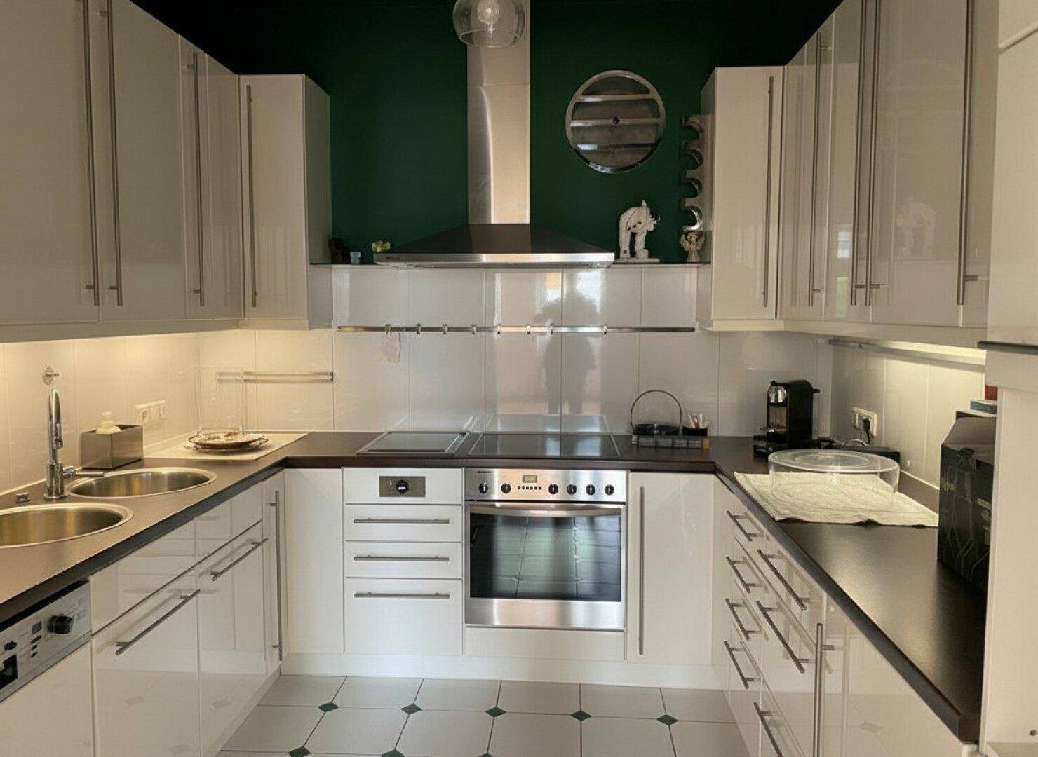Moderne Einbauküche mit weißen Hochglanzfronten, dunkler Arbeitsplatte und grüner Akzentwand.