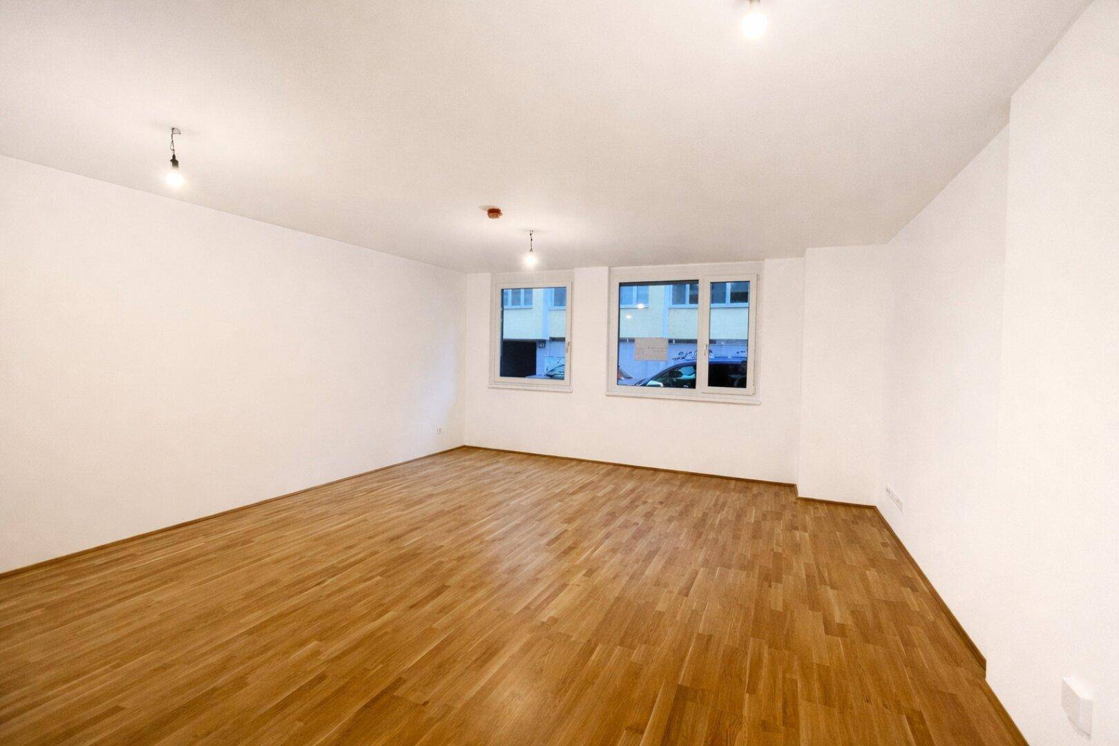 Geräumiger, heller Raum mit Parkettboden und zwei Fenstern, ideal für Wohn- oder Schlafzimmer.