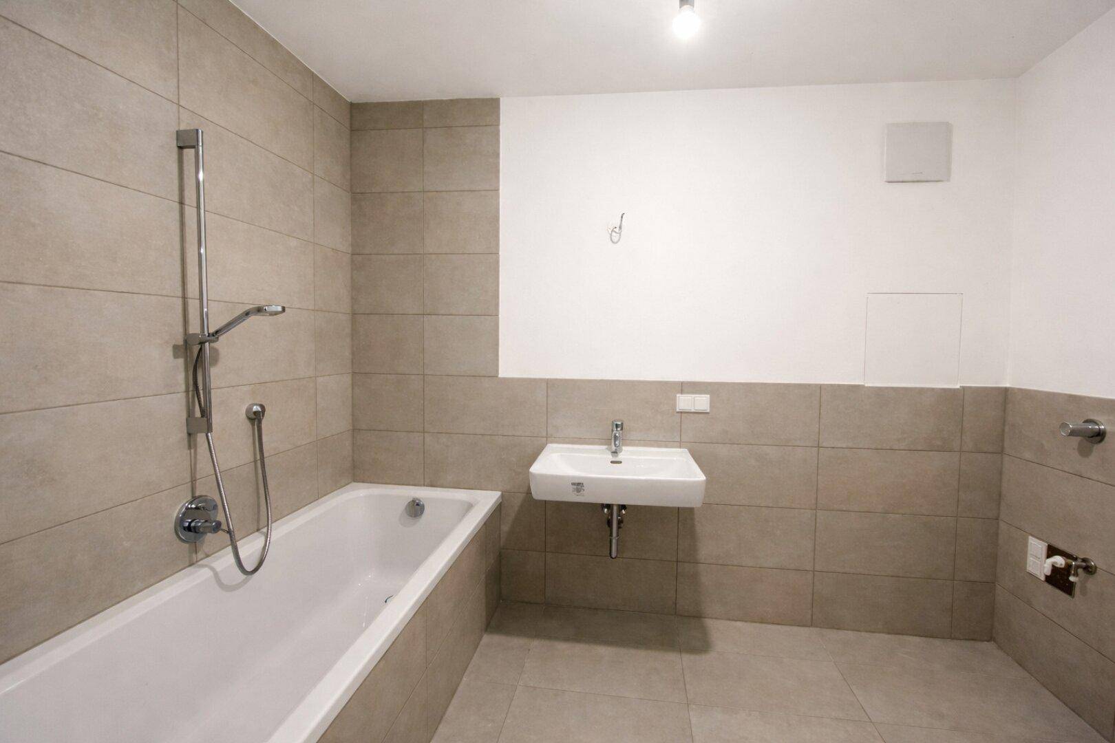 Modernes Badezimmer mit Badewanne, Einzelwaschbecken und hellen Fliesen an Wänden und Boden.
