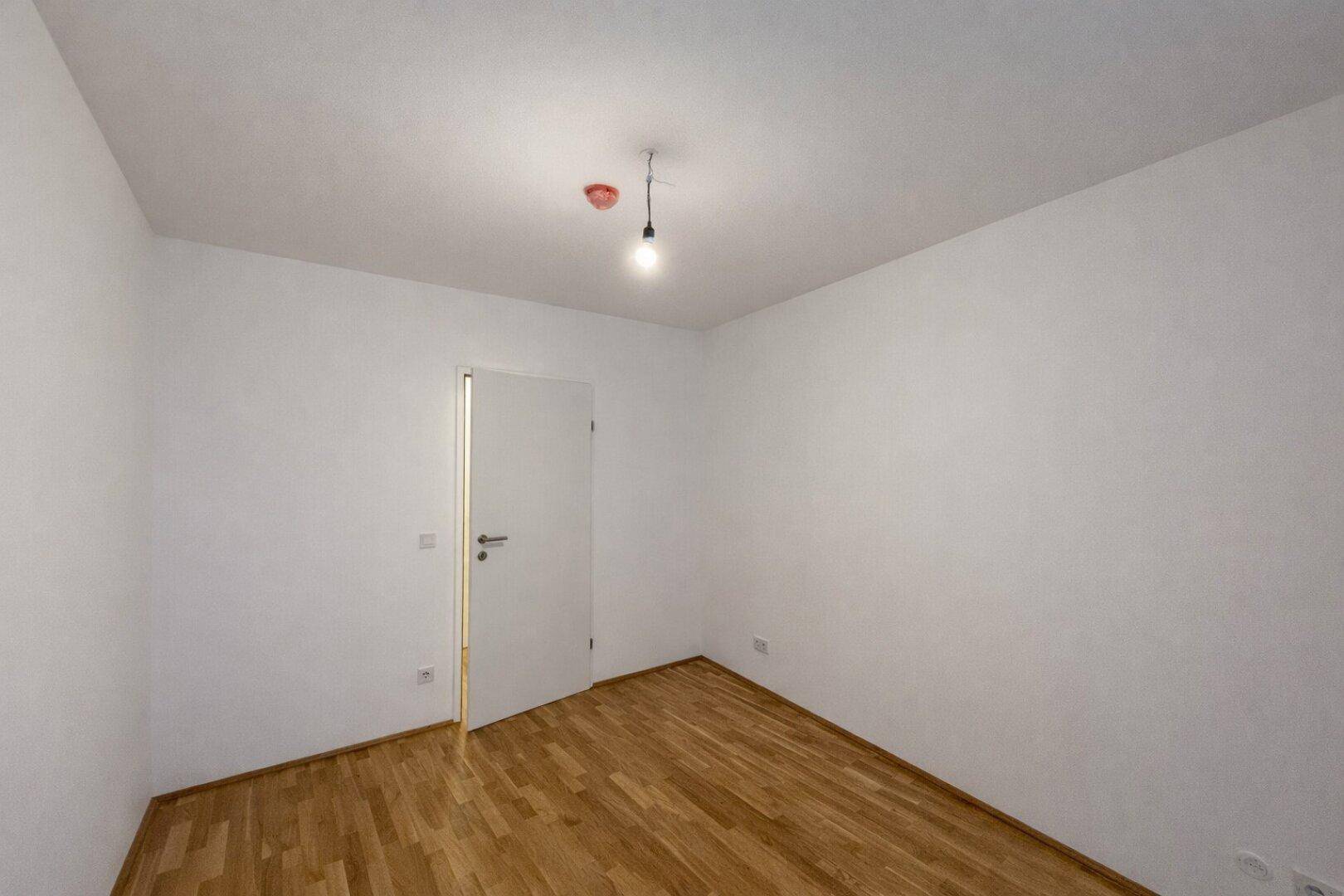 Unmöbliertes Zimmer mit Parkettboden und weißer Tür, bietet vielseitige Nutzungsmöglichkeiten.