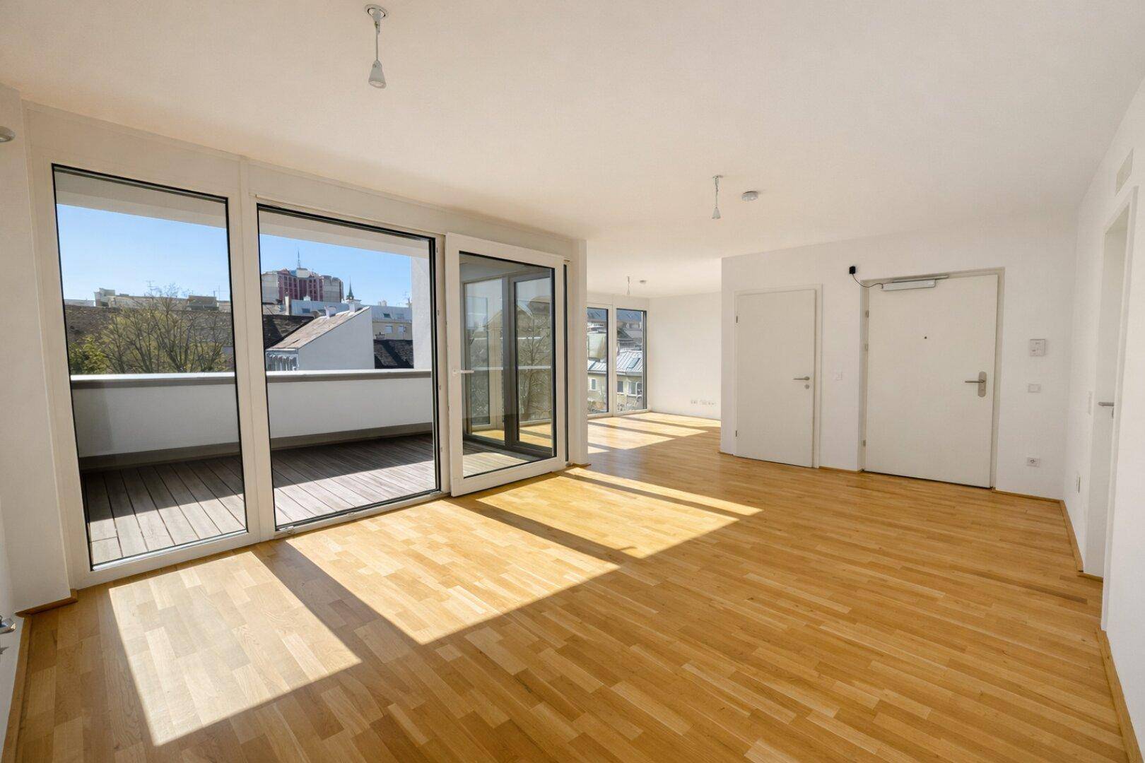 Lichtdurchfluteter Wohnbereich mit hellem Parkettboden und Zugang zu einem sonnigen Balkon.