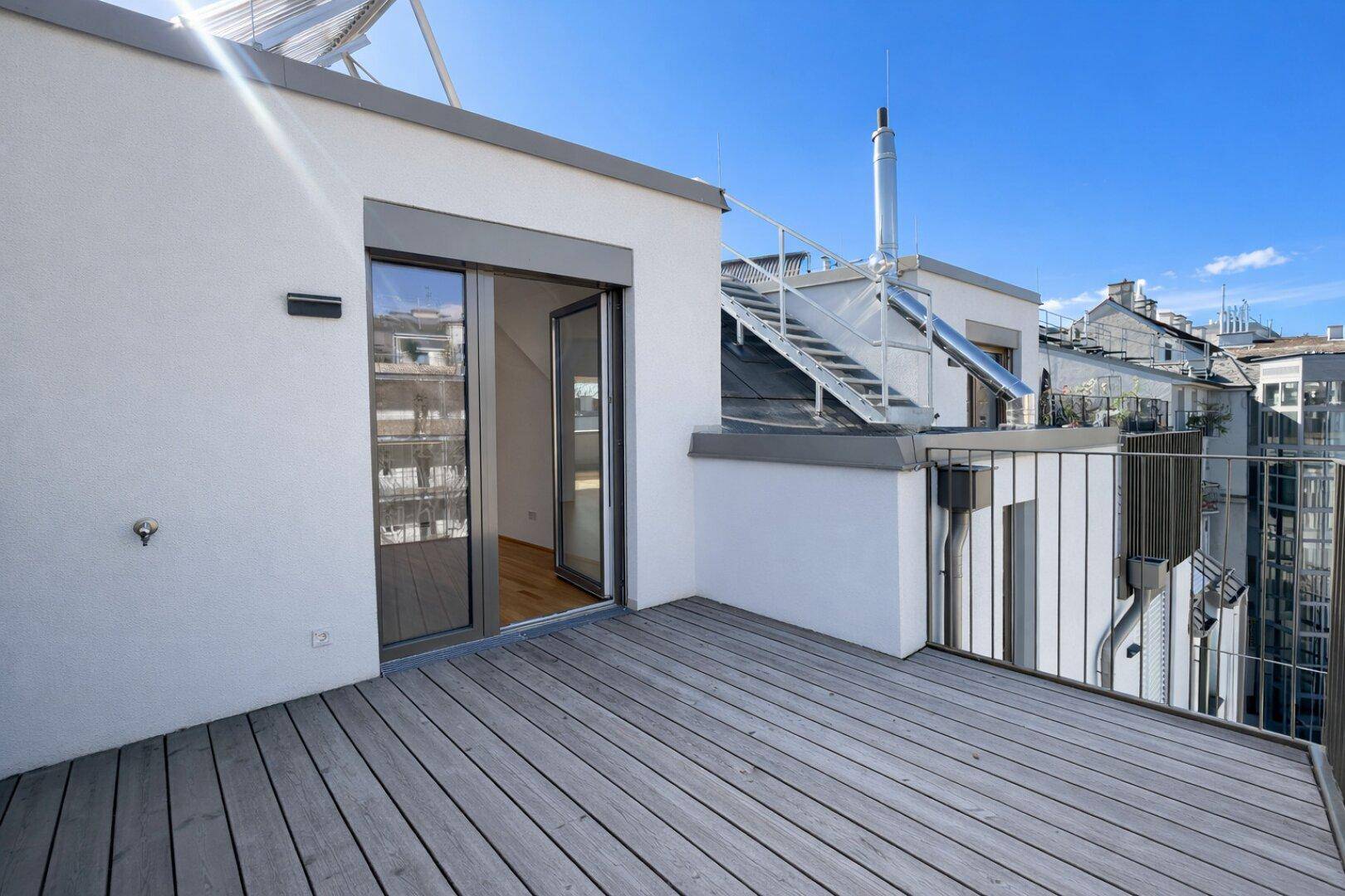 Sonniger Balkon mit Holzboden und Blick auf die Dächer der Stadt.