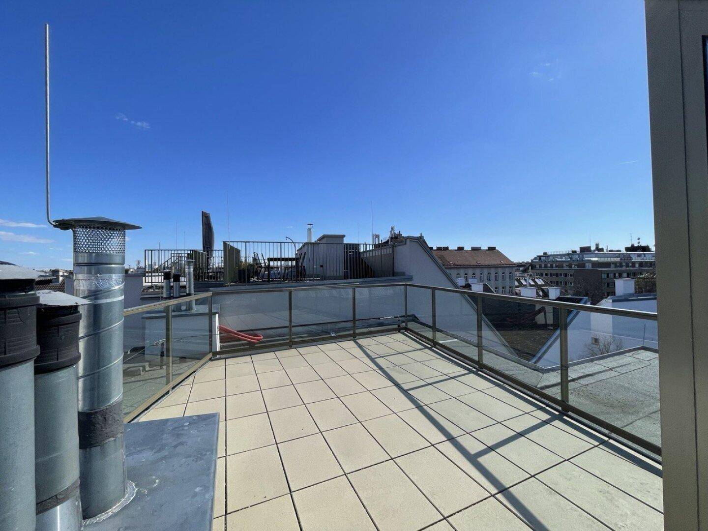 Weitläufige Dachterrasse mit Fliesenboden und Panoramablick über die umliegenden Dächer.