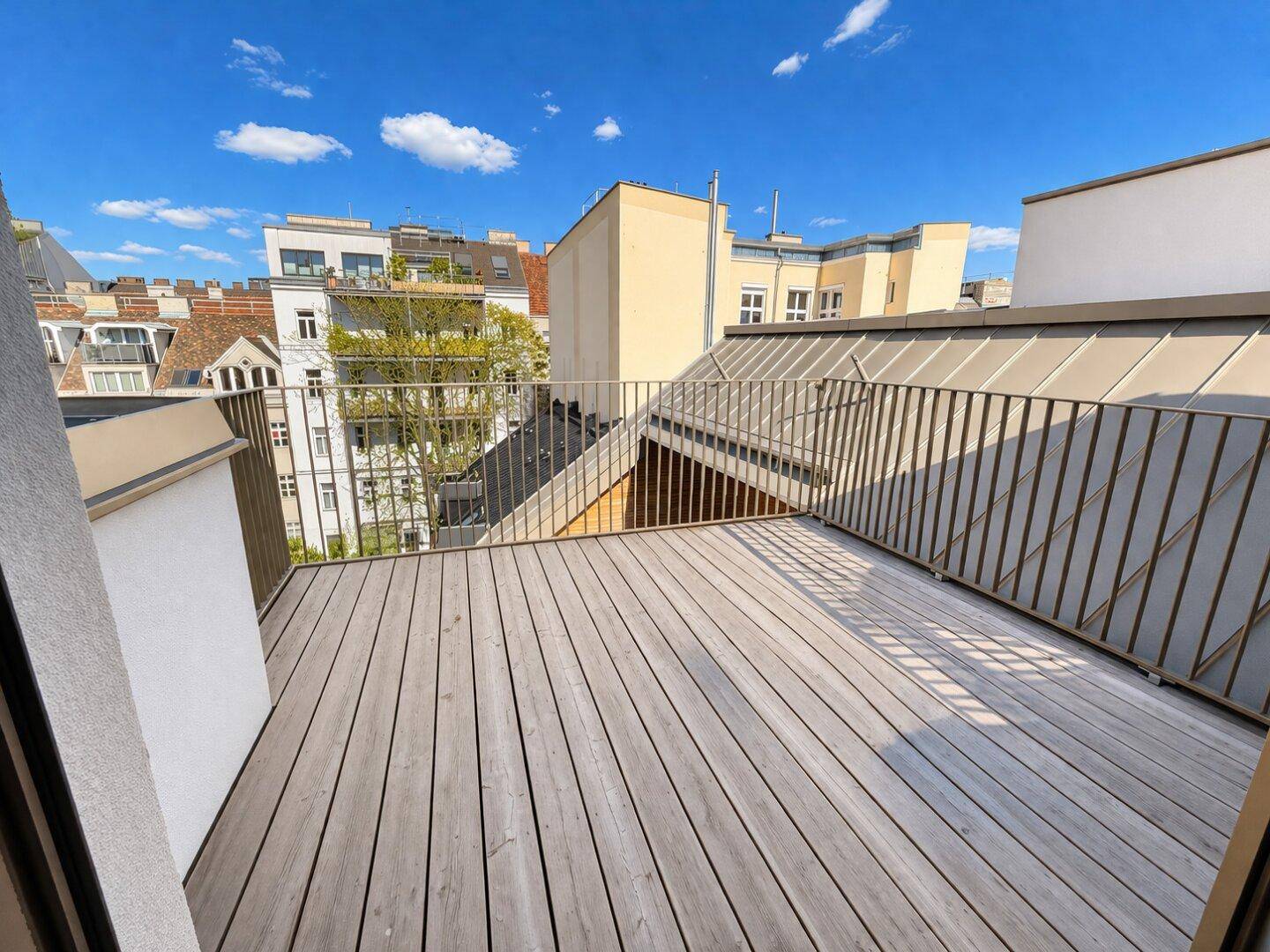 Geräumiger Balkon mit Holzdielenboden und Blick auf die umliegenden Gebäude.