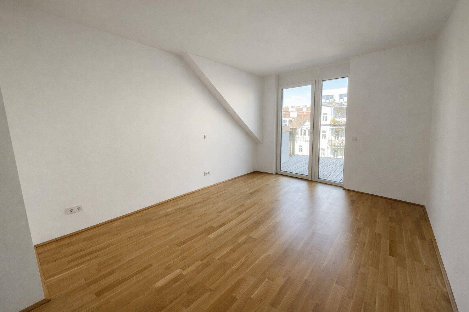 Leeres Schlafzimmer mit Parkettboden, Dachschräge und Zugang zu einem Außenbereich.