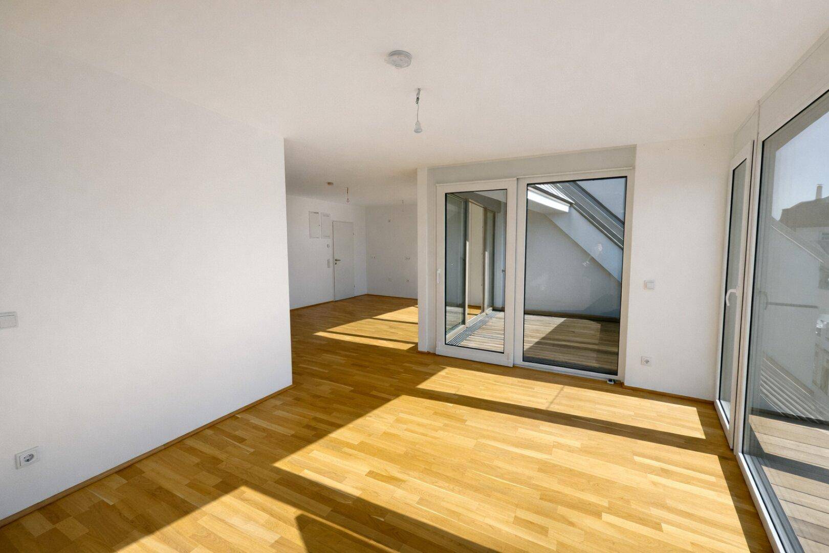 Geräumiger Wohnbereich mit Parkettboden und großen Fenstern, die viel Tageslicht hereinlassen.