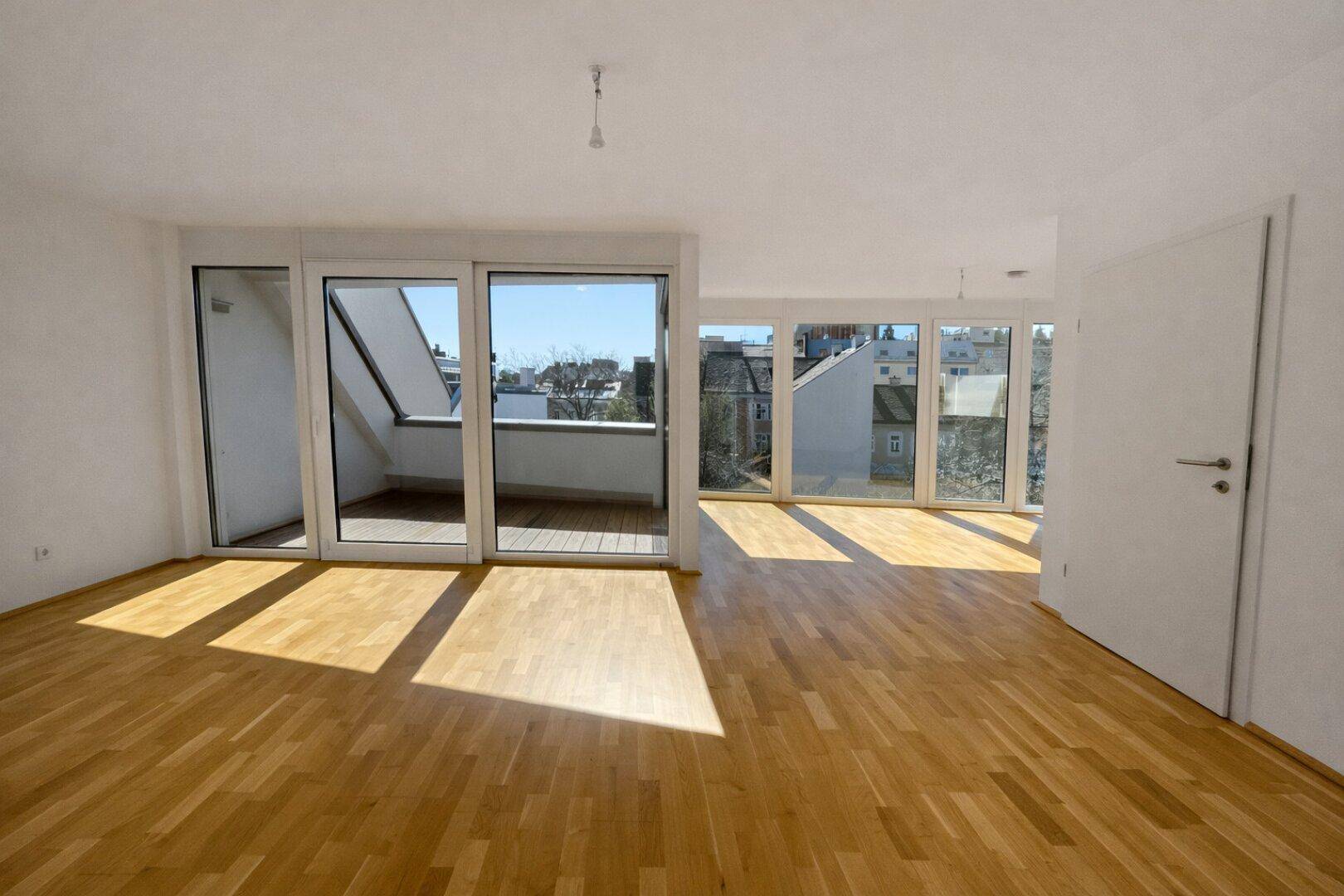 Heller Wohnbereich mit Parkettboden und großen Schiebetüren, die auf einen Balkon führen.