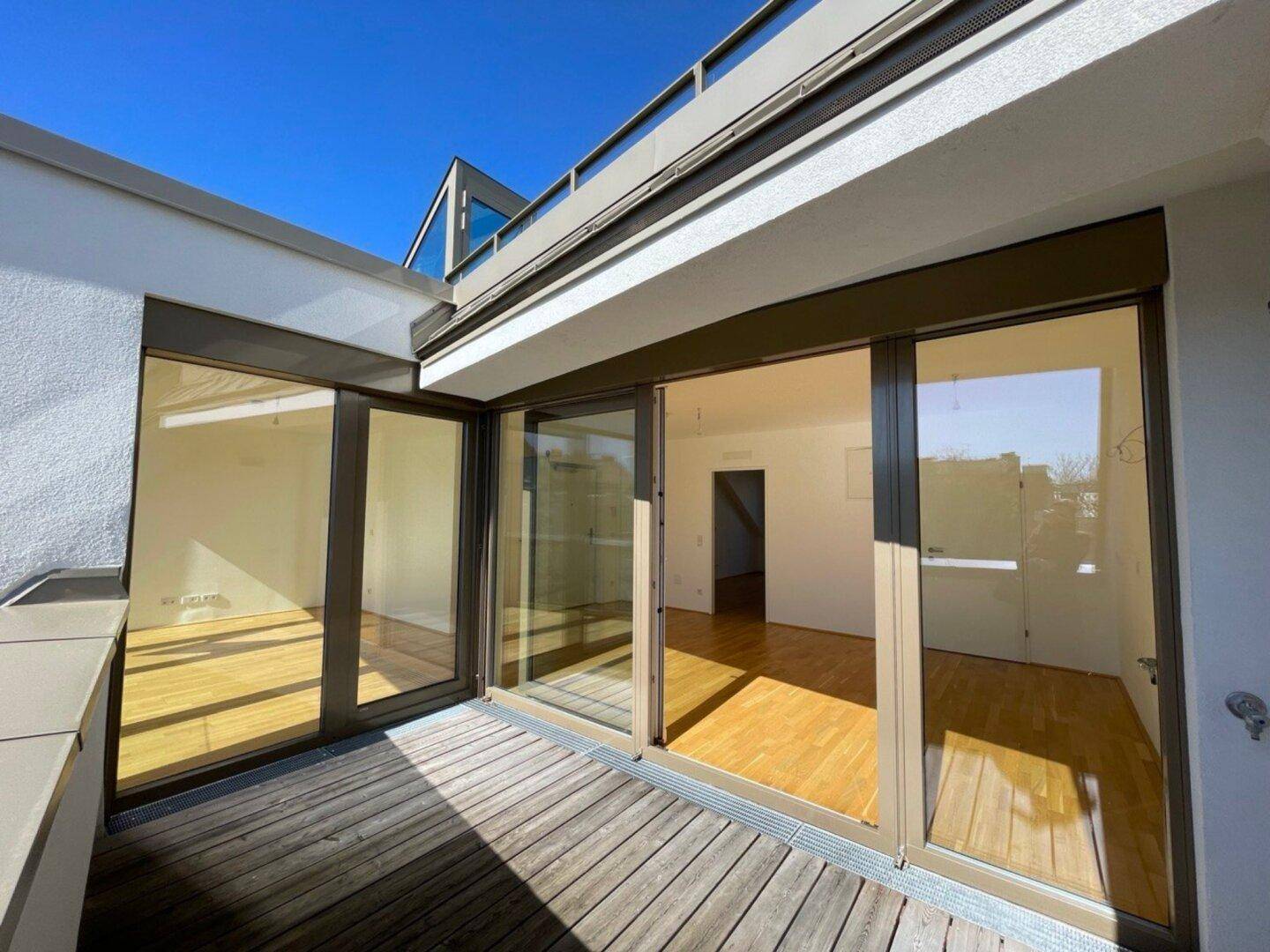 Balkon mit Holzboden und großen Glasfronten, die viel Licht in den Innenraum lassen.