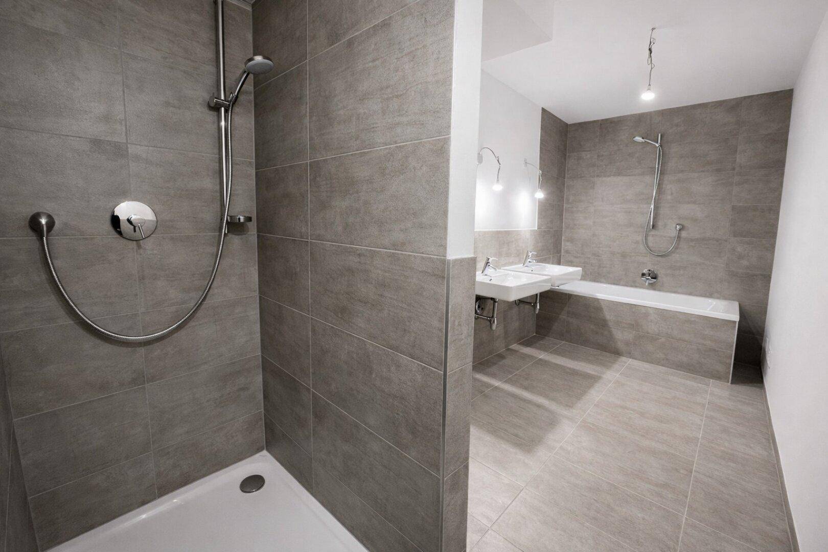 Modernes Badezimmer mit grauen Fliesen, Doppelwaschbecken, Dusche und Badewanne.