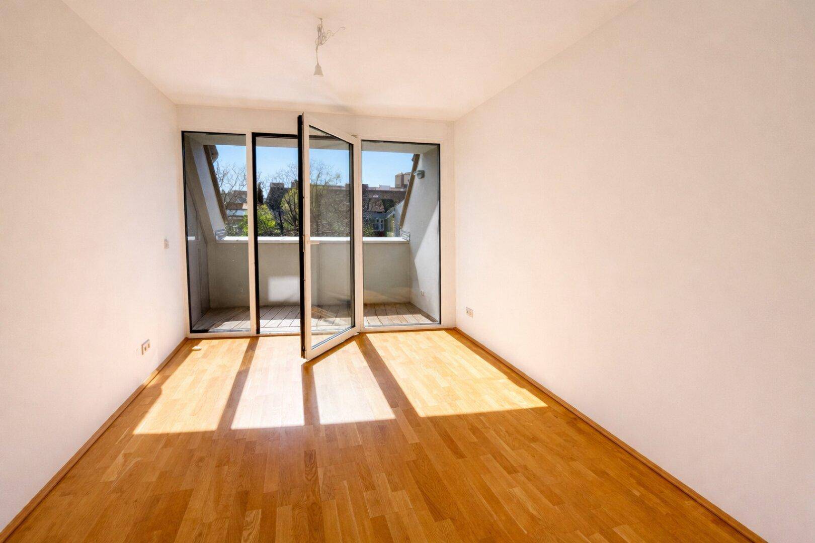 Helles Schlafzimmer mit Parkettboden und Zugang zu einem französischen Balkon, ideal für natürliches Licht.