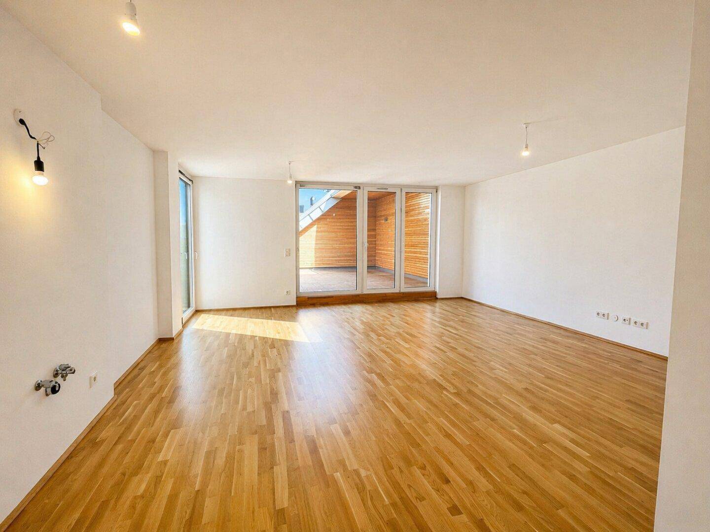 Lichtdurchfluteter Wohnraum mit Holzboden und großen Fenstern, die Zugang zur Terrasse bieten.
