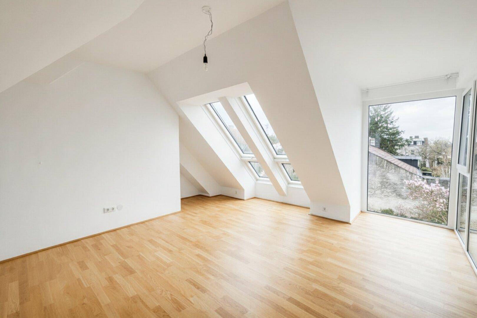 Heller Dachgeschossraum mit Holzboden, schrägen Wänden und Dachfenstern, die viel Licht hereinlassen.