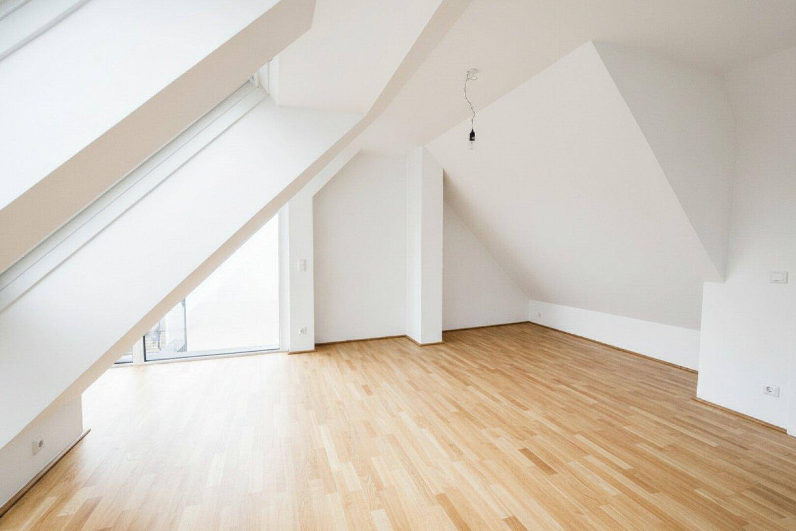 Geräumiger Dachgeschossraum mit Holzboden, schrägen Wänden und Zugang zu einem Außenbereich.