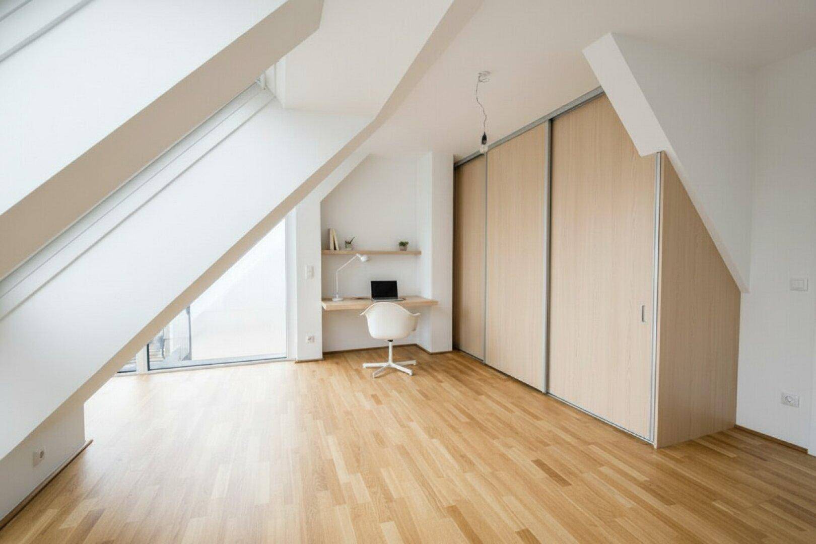 Heller Dachgeschossraum mit Holzboden, integriertem Schreibtisch und praktischen Schiebetürenschränken.