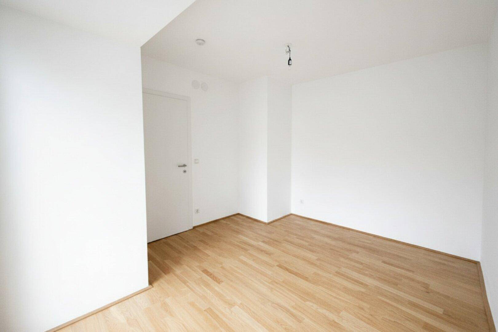 Schlichter, heller Raum mit Holzboden und weißen Wänden, bereit zur individuellen Einrichtung.