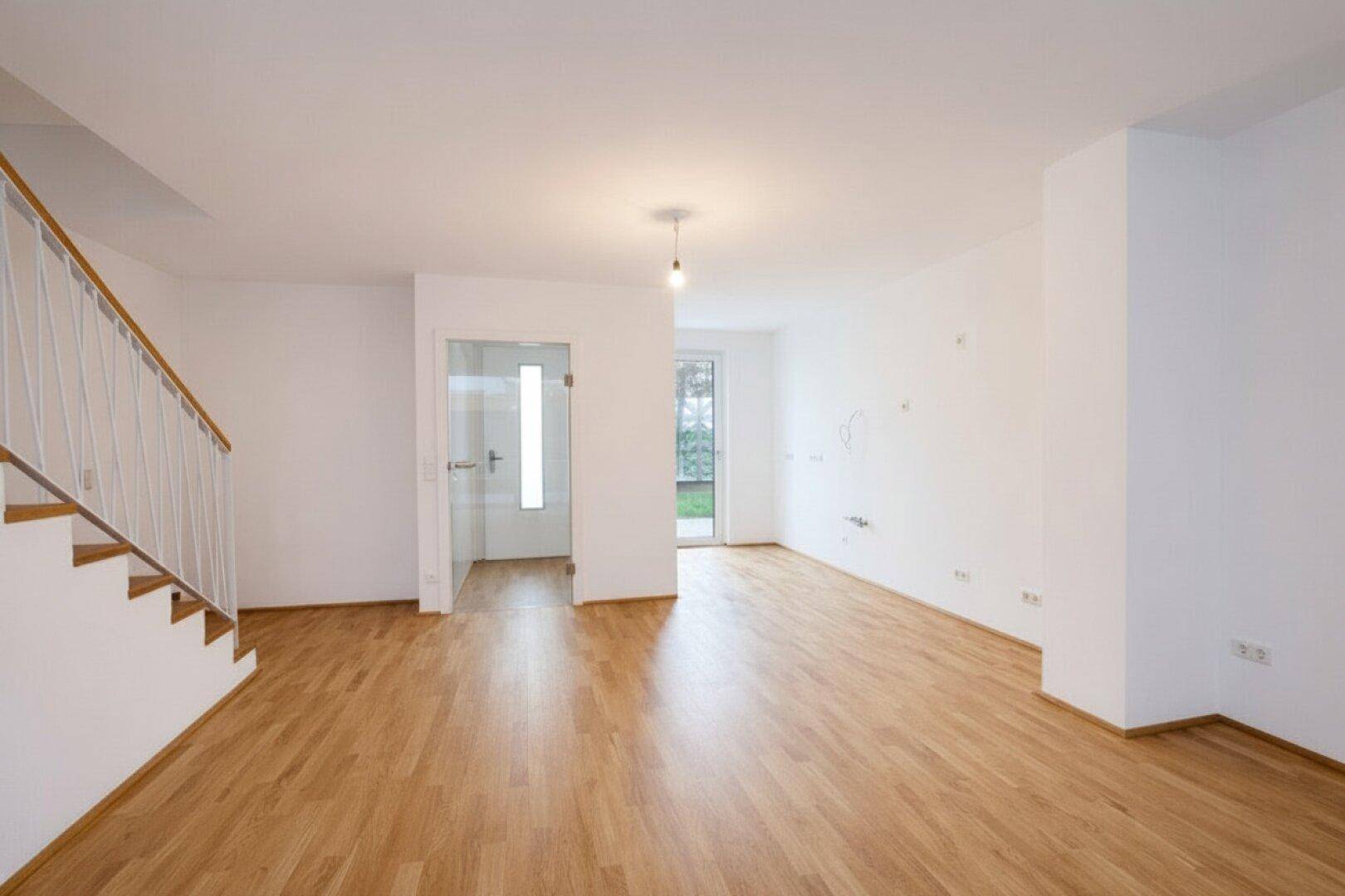 Geräumiger, heller Wohnbereich mit Holzboden, weißen Wänden und Treppenaufgang, bereit zur individuellen Gestaltung.