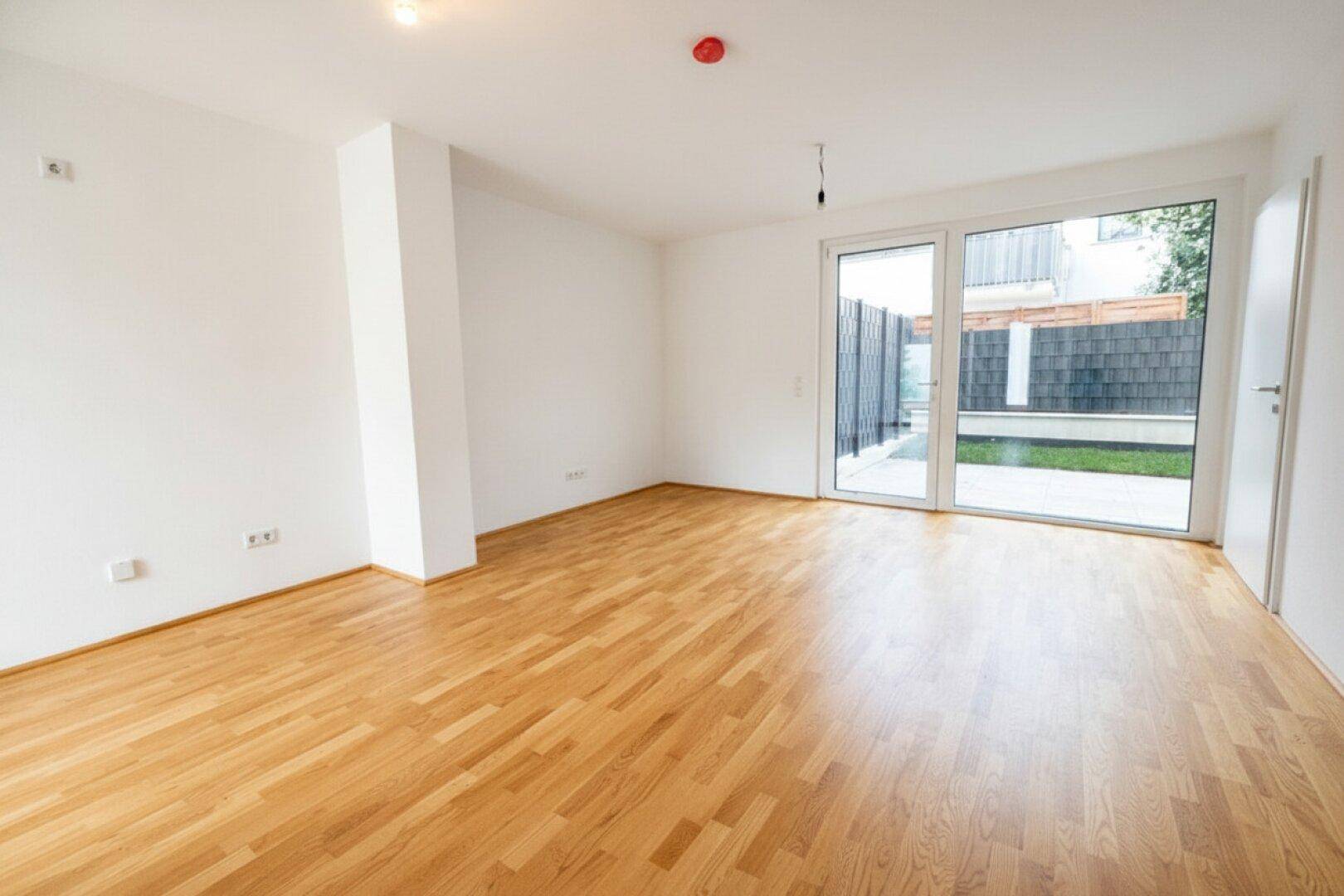 Heller Raum mit Holzboden und großen Glastüren, die Zugang zu einem Außenbereich bieten.
