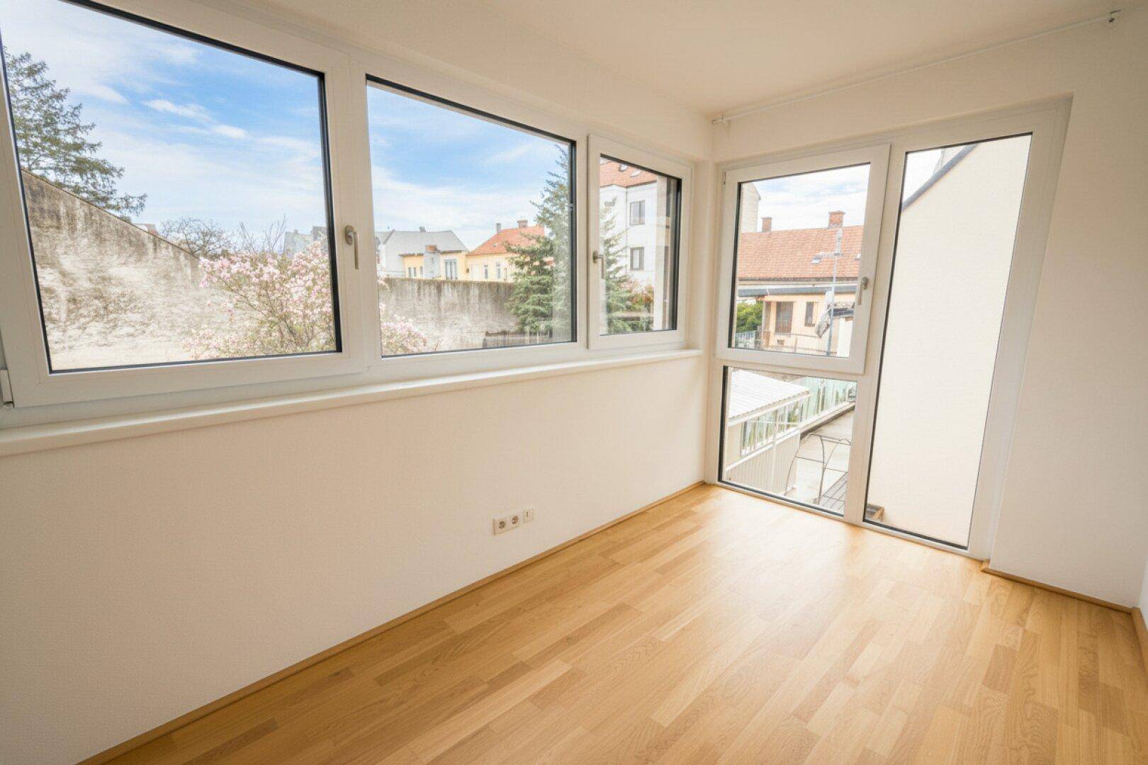 Heller Raum mit Holzboden und großen Fenstern, die einen Blick auf die Umgebung ermöglichen.