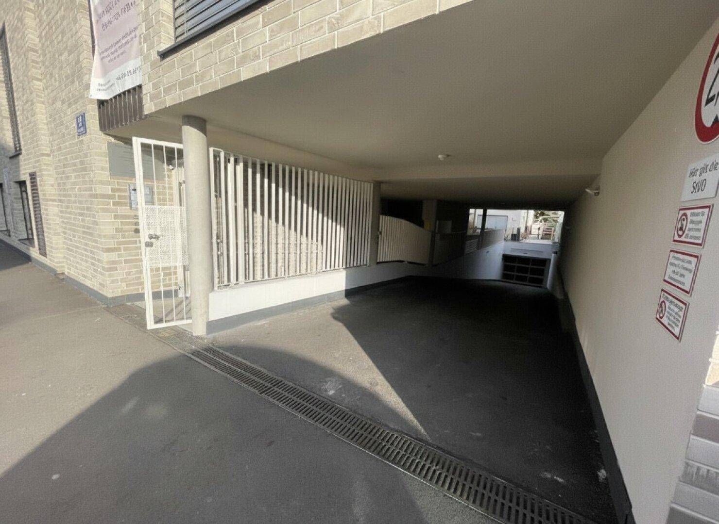Einfahrt zu einer Tiefgarage mit Rampe und Sicherheitsgittern.
