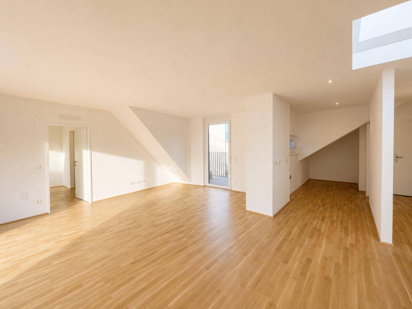 Lichtdurchfluteter Wohnbereich mit hellem Holzboden und Zugang zu einem kleinen Balkon.